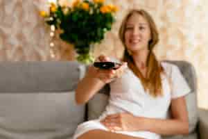 Foto gratuita donna sorridente con telecomando tv in mano guardando la tv mentre seduto sul divano in salotto