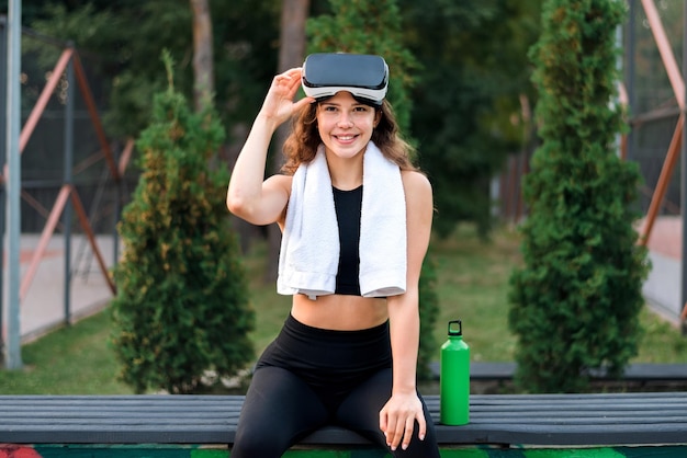 Free photo smiling woman with vr headset towel and water bottle in a tracksuit looking into the camera