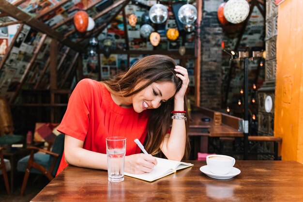 机の上にコーヒーの一杯で日記のスケジュールを書く笑顔の女性