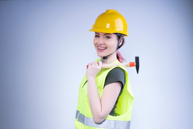 Улыбающаяся женщина в желтом шлеме стоит с молотком на плече