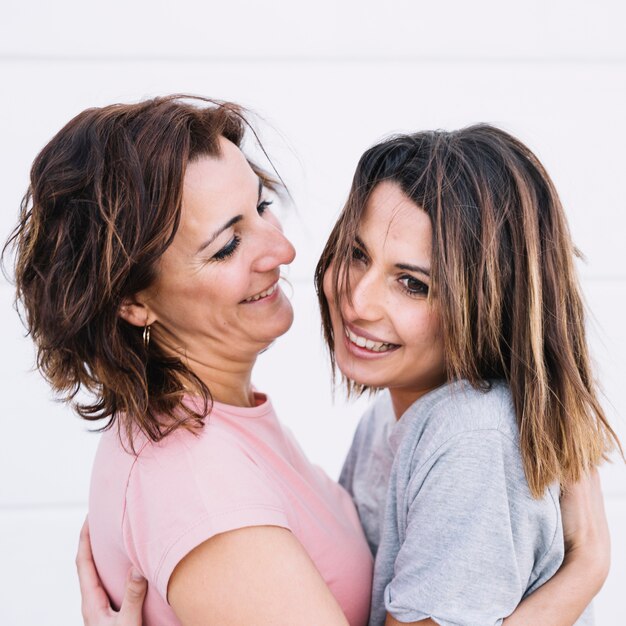 Smiling women hugging near white wall