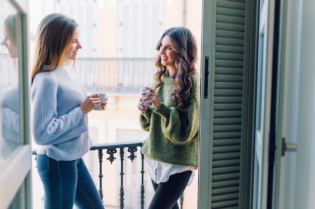 Smiling women with mugs on balcony