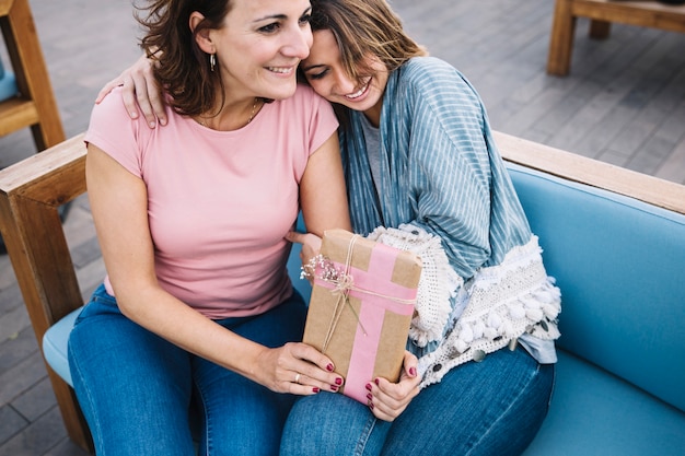 Free photo smiling women with present hugging on couch