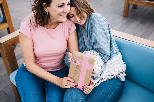 Smiling women with present hugging on couch