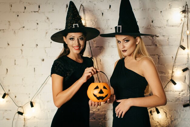 Smiling women with pumpkins at illuminated brickwall