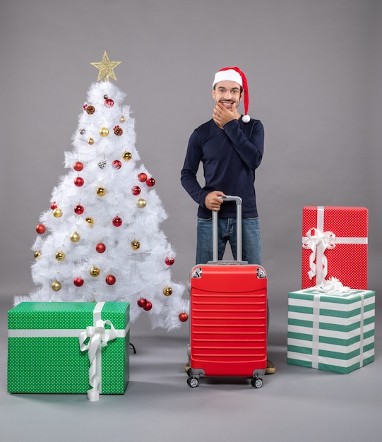 smiling xmas man holding red valise near white xmas tree with colorful xmas toys on