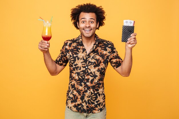 Smiling young african man drinking cocktail and holding tickets.