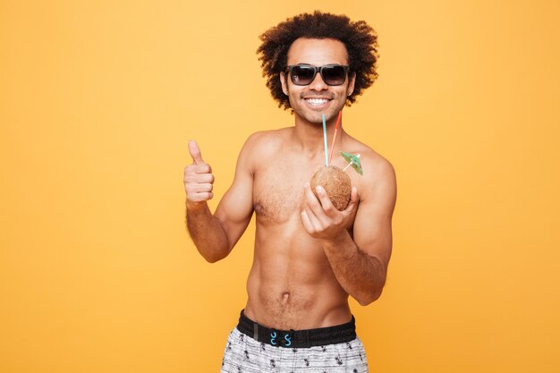 Smiling young african man drinking cocktail and showing thumbs up.