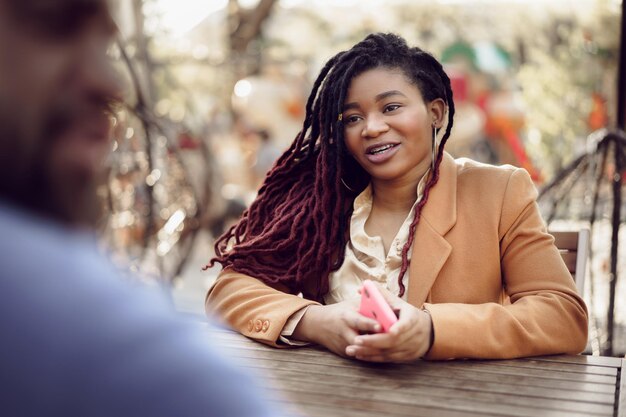 Smiling young african woman sitting at a table in cafe with caucasian man and having a talk