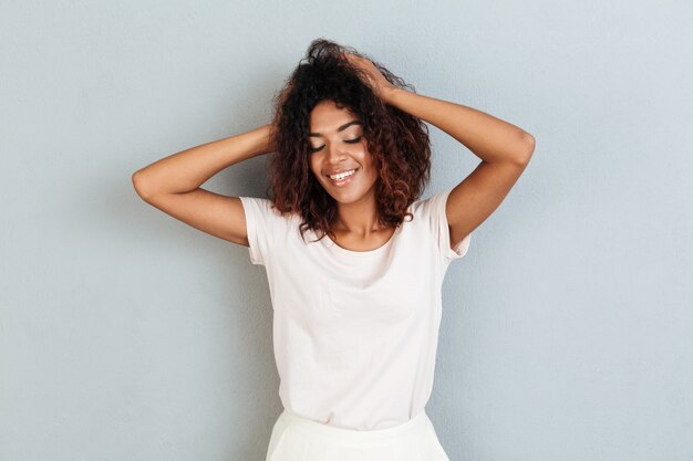 Smiling young african woman standing over grey wall.