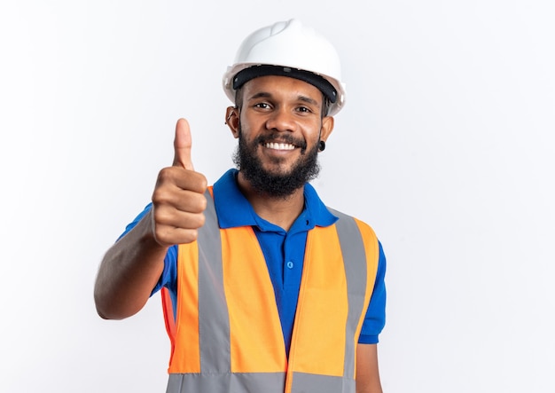 Smiling young afro-american builder man in uniform with safety helmet thumbing up isolated on white background with copy space