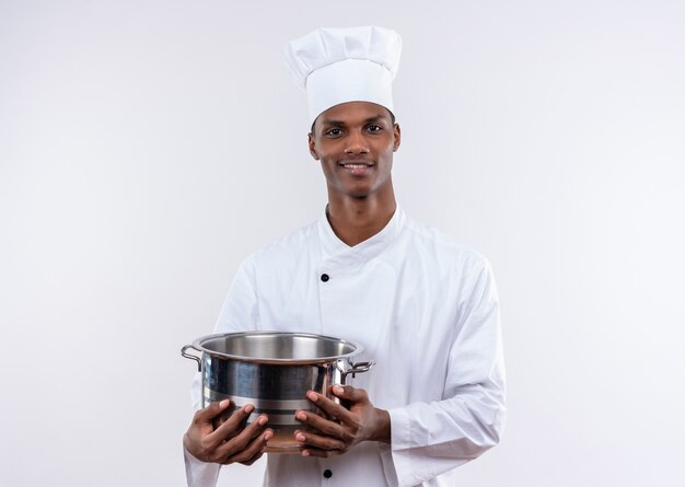 요리사 유니폼에 웃는 젊은 아프리카 계 미국인 요리사는 냄비를 보유하고 복사 공간이 격리 된 흰색 배경에 카메라를 찾습니다