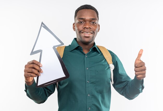 Smiling young afro-american student with backpack holding arrow pointing up and thumbing up 