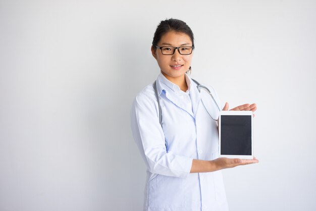 Smiling young Asian female doctor showing tablet computer screen. 