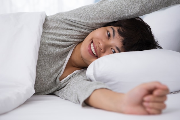 Sorridente giovane asiatica ragazza svegliarsi nel letto