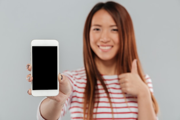 Free photo smiling young asian woman showing display of phone