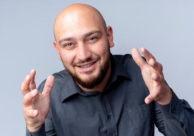 Smiling young bald call center man keeping hands in air looking at front isolated on white wall