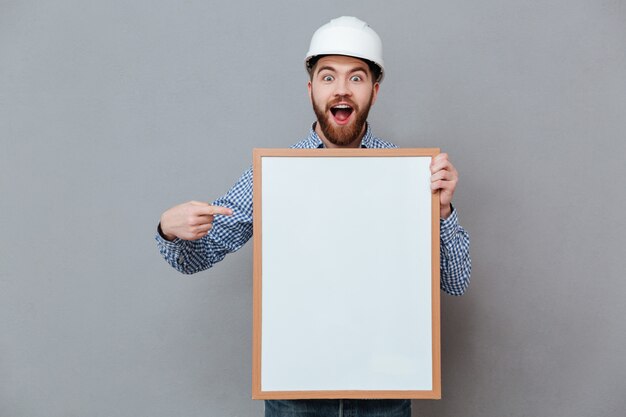 Smiling young bearded builder holding blank board