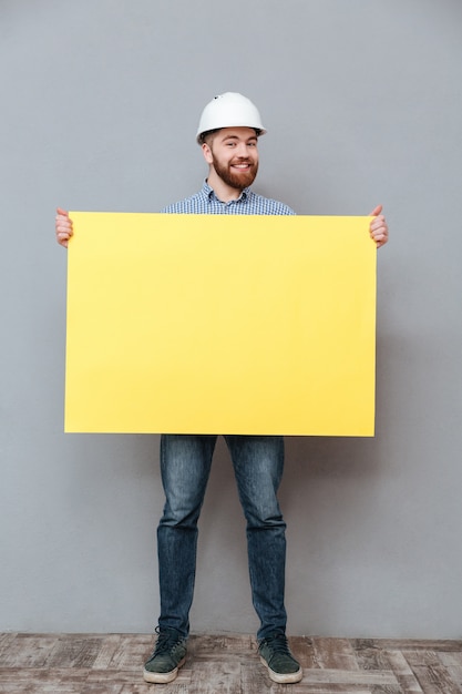 Smiling young bearded builder holding blank board