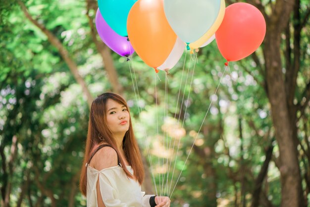 Smiling young beautiful asian women with long brown hair in the park. With rainbow-colored air balloons in her hands.sunny and positive energy of nature.