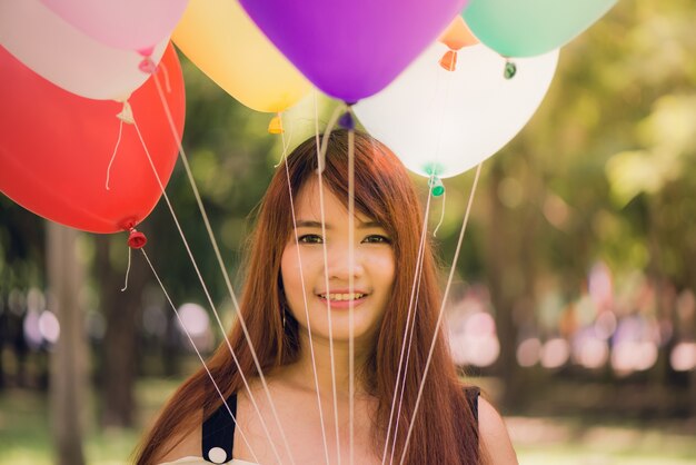 Smiling young beautiful asian women with long brown hair in the park. With rainbow-colored air balloons in her hands.sunny and positive energy of nature.