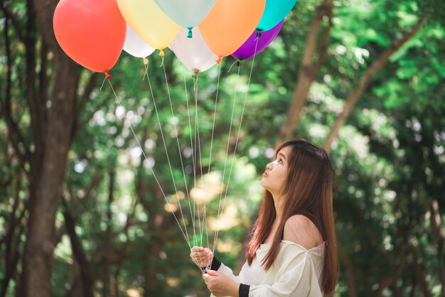 Smiling young beautiful asian women with long brown hair in the park. With rainbow-colored air balloons in her hands.sunny and positive energy of nature.