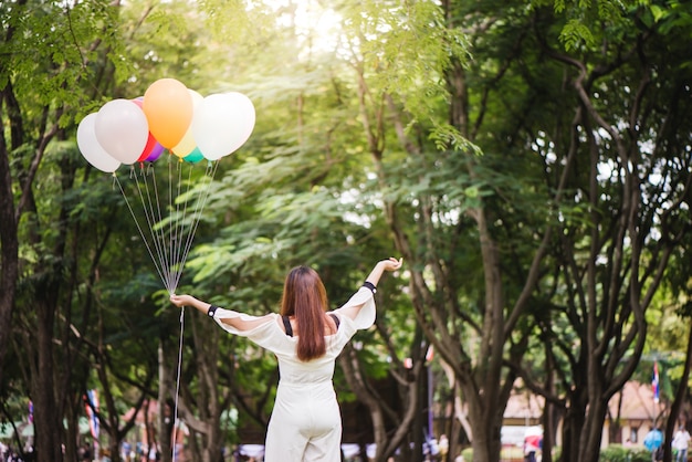 Smiling young beautiful asian women with long brown hair in the park. With rainbow-colored air balloons in her hands.sunny and positive energy of nature.