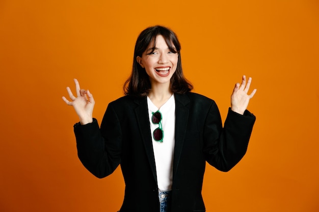 Smiling young beautiful female wearing black jacket isolated on orange background