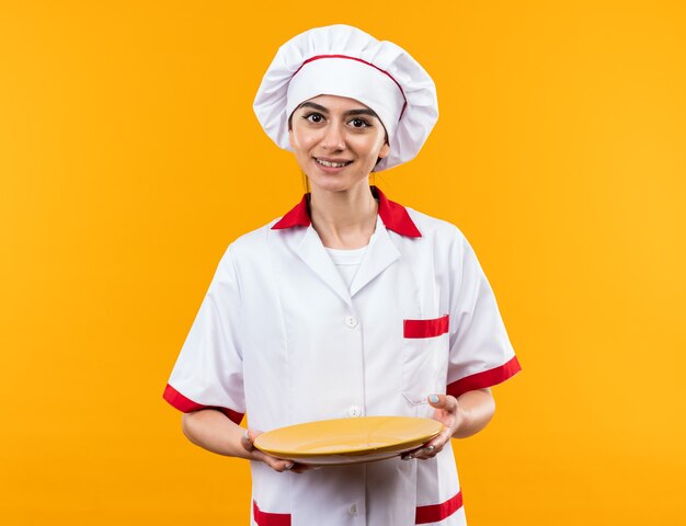 Sorridente giovane bella ragazza in uniforme da chef che tiene piatto