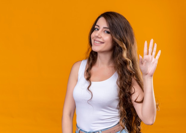 Foto gratuita giovane bella ragazza sorridente che gesturing ciao sullo spazio arancione isolato con lo spazio della copia