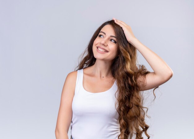 Smiling young beautiful girl looking at left side with hand on head  with copy space