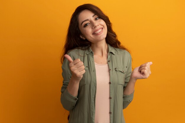 Smiling young beautiful girl wearing olive green t-shirt showing thumbs up isolated on yellow wall