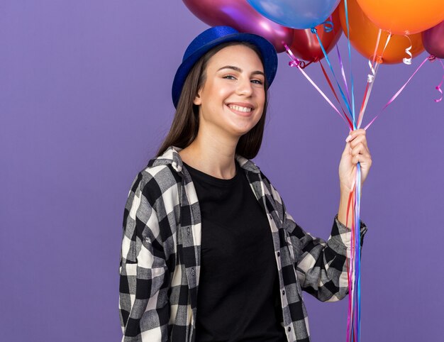 Smiling young beautiful girl wearing party hat holding balloons 