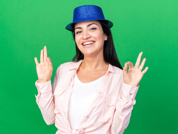 Smiling young beautiful girl wearing party hat showing okay gesture 