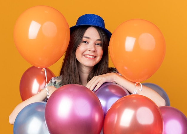 Улыбающаяся молодая красивая девушка в партийной шляпе, стоящая за воздушными шарами