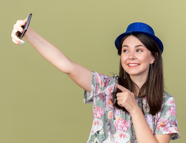 파티 모자를 쓰고 웃고 있는 아름다운 소녀는 전화로 셀카 포인트를 찍습니다