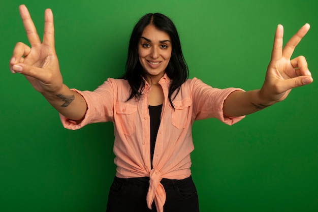 Free photo smiling young beautiful girl wearing pink t-shirt showing peace gesture isolated on green