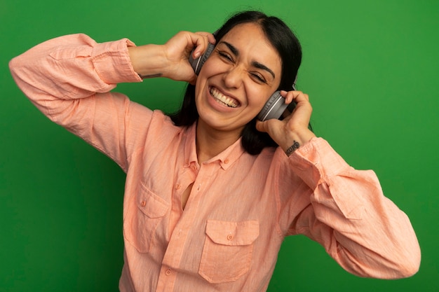 녹색 벽에 고립 된 헤드폰 핑크 티셔츠를 입고 젊은 아름 다운 소녀 미소