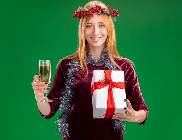 녹색 배경에 고립 된 선물 상자와 샴페인 잔을 들고 목에 화 환과 갈 랜드와 빨간 드레스를 입고 웃는 젊은 아름 다운 소녀