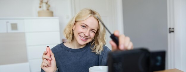 Smiling young beautiful lifestyle blogger girl records a beauty vlog in her room using professional