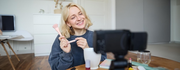 Smiling young beautiful lifestyle blogger girl records a beauty vlog in her room using professional