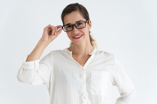 Smiling young beautiful woman adjusting glasses and looking at camera.