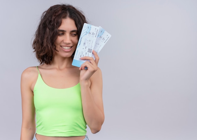 Smiling young beautiful woman holding airplane tickets on isolated white wall with copy space