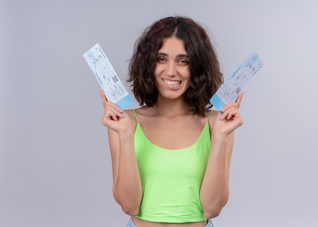 Smiling young beautiful woman holding airplane tickets on isolated white wall