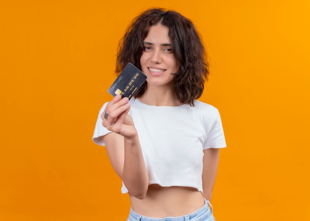 Smiling young beautiful woman holding card on isolated orange wall with copy space