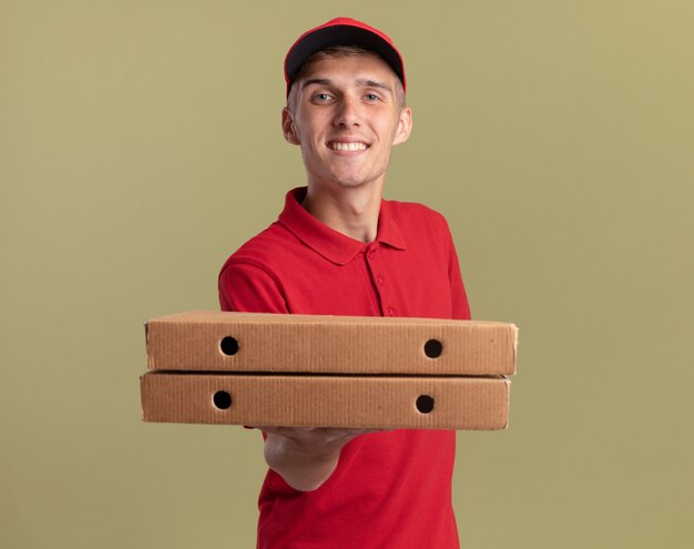 Smiling young blonde delivery boy holding pizza boxes looking at camera