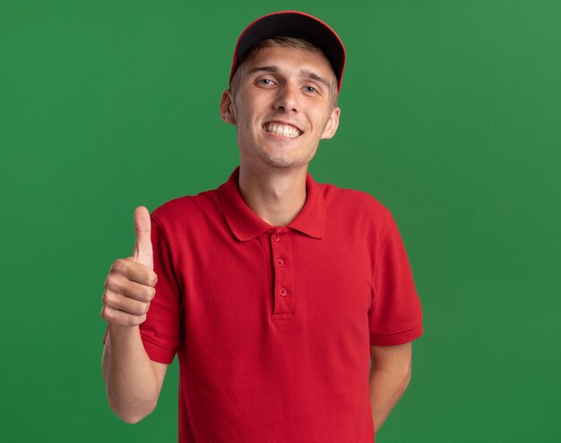 Smiling young blonde delivery boy thumbing up on green 