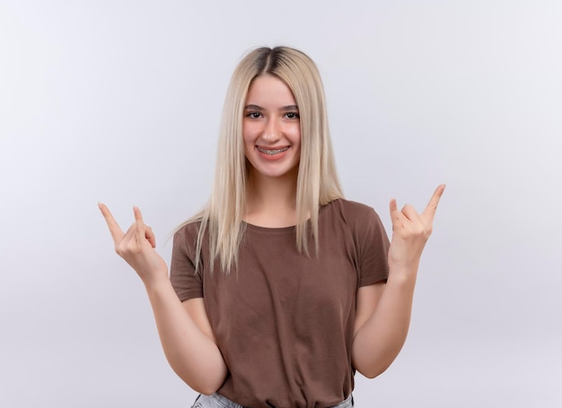 Smiling young blonde girl in dental braces doing rock sign on isolated white space