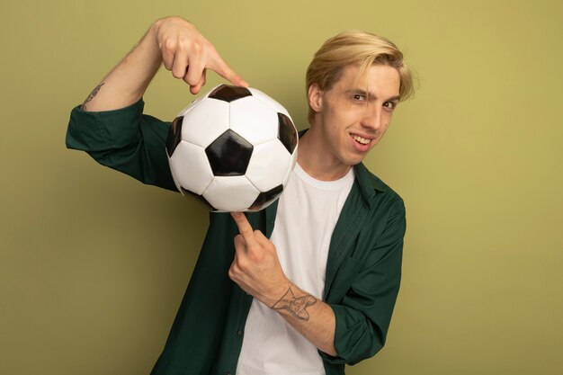 Улыбающийся молодой блондин в зеленой футболке с мячом на пальцах