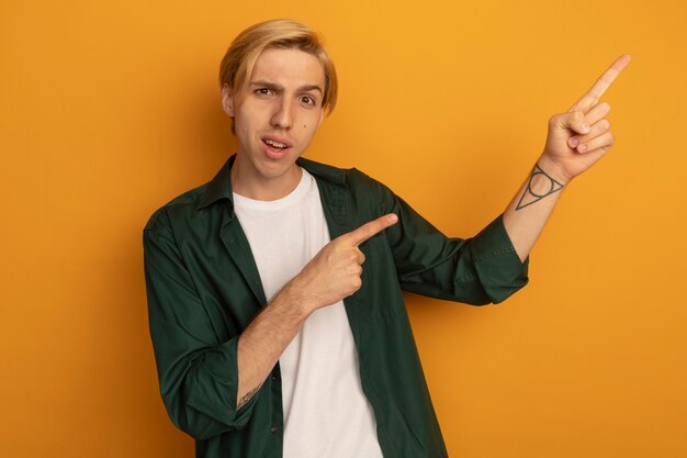 Smiling young blonde guy wearing green t-shirt points at side